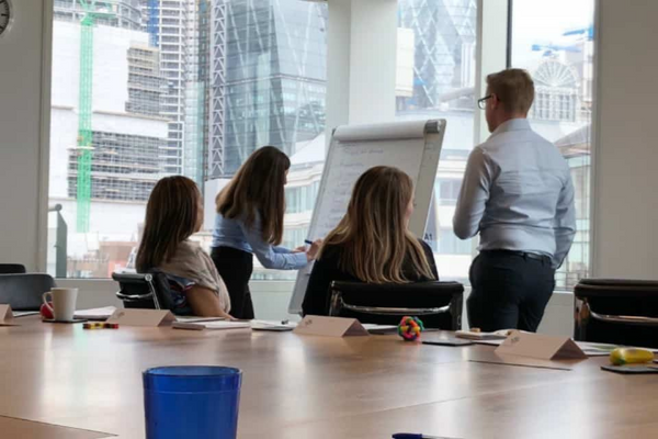 Two people present to a small group using a whiteboard in a boardroom